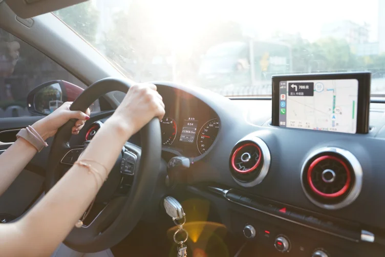 Pessoa dirigindo um carro com as mãos no volante e a navegação aberta no painel.