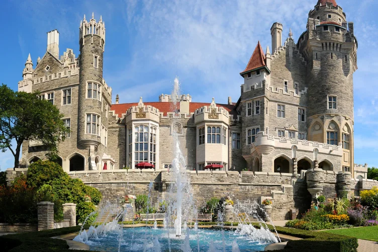 Vista do Castelo Casa Loma com fonte e jardins na frente, sob um céu azul.