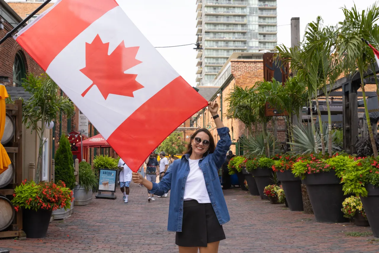 Mulher sorrindo, segurando uma grande bandeira do Canadá no Distillery District em Toronto.