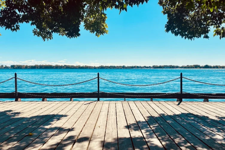 Deck de madeira à beira do Lago Ontário com vista para a água azul em um dia ensolarado.