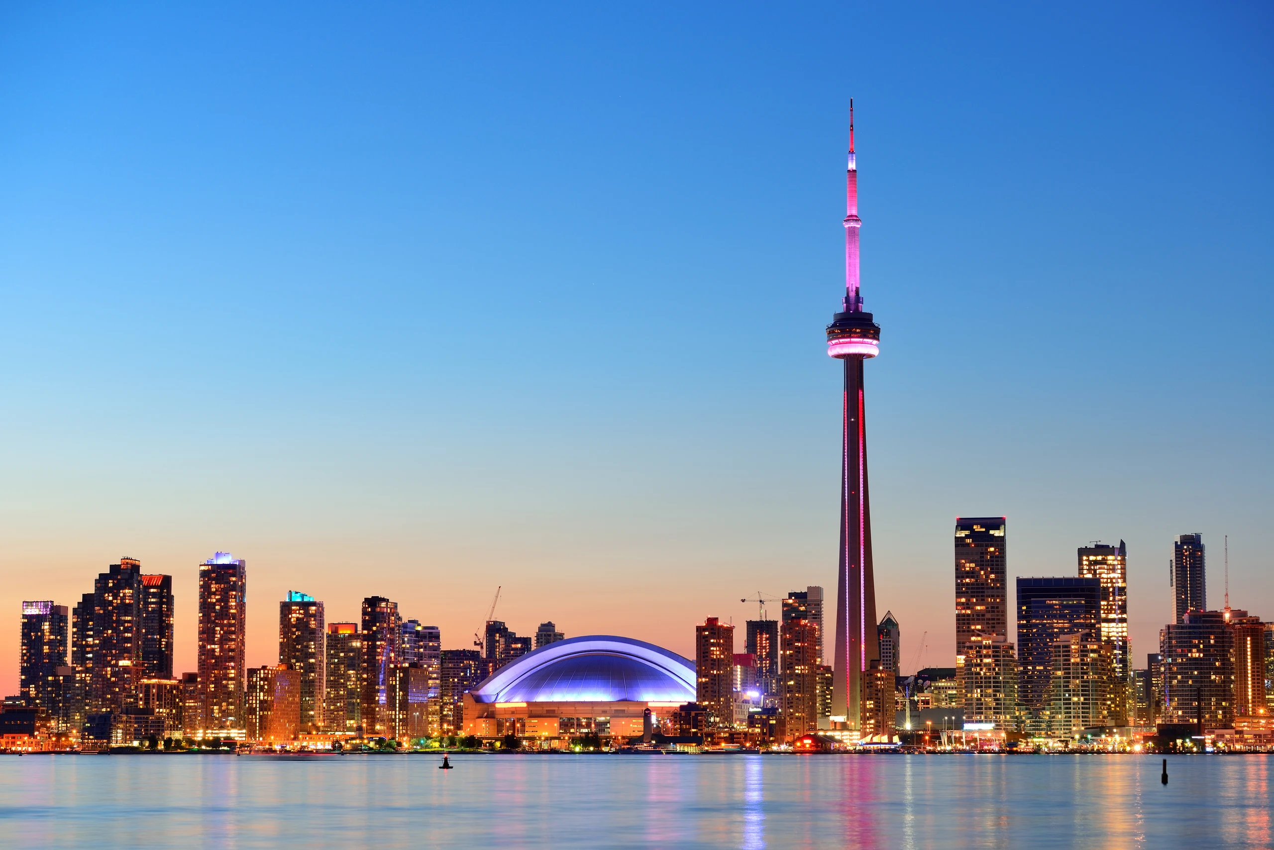 Skyline de Toronto ao anoitecer, com a CN Tower iluminada junto ao Lago Ontário.