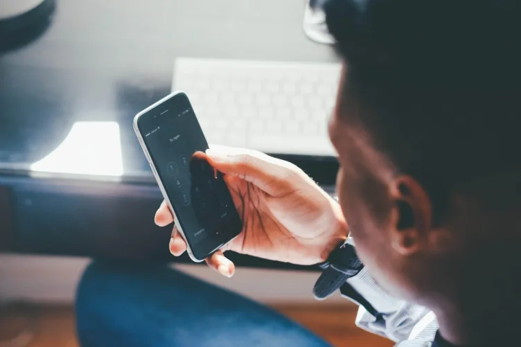 Pessoa usando smartphone próximo a um teclado, com foco na mão segurando o aparelho.