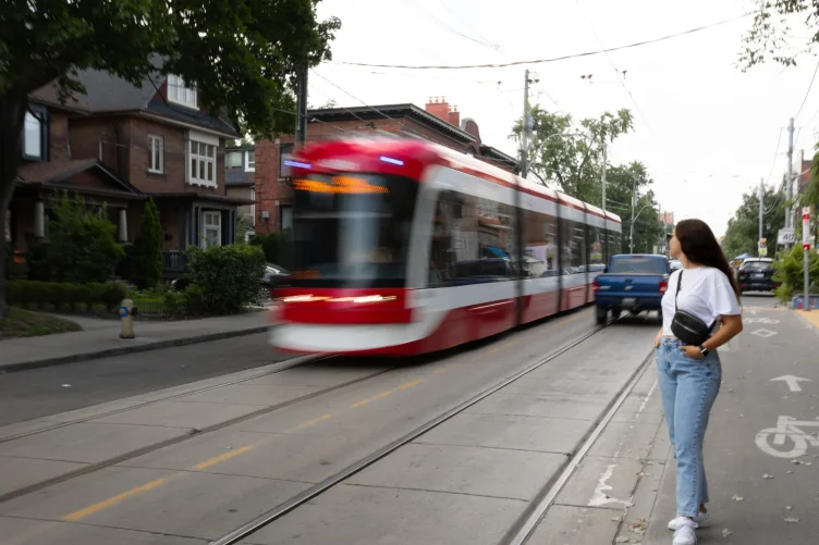 Mulher aguardando enquanto um bondinho moderno passa em um bairro residencial de Toronto.