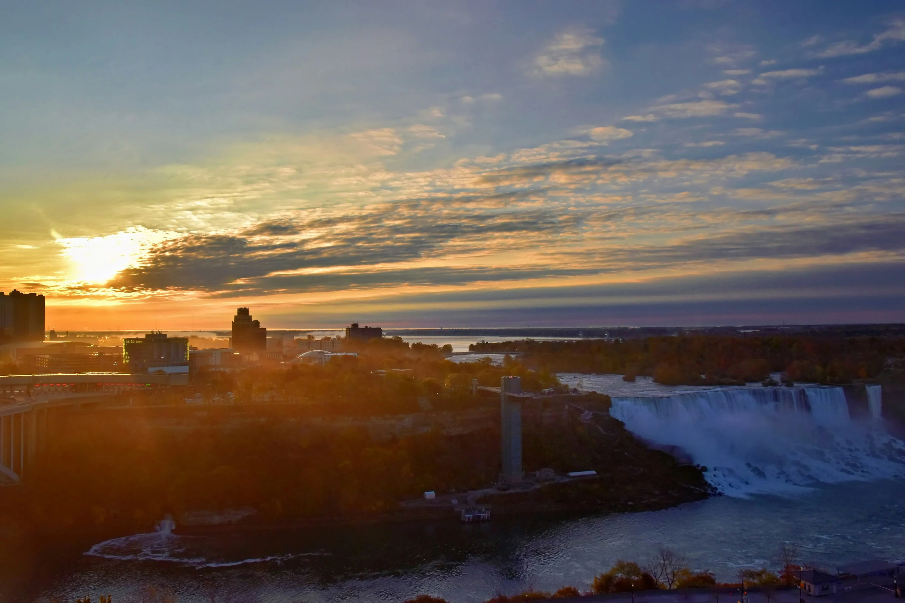 Cataratas de Niagara ao amanhecer, com nuvens douradas e água azul sob a luz do sol.
