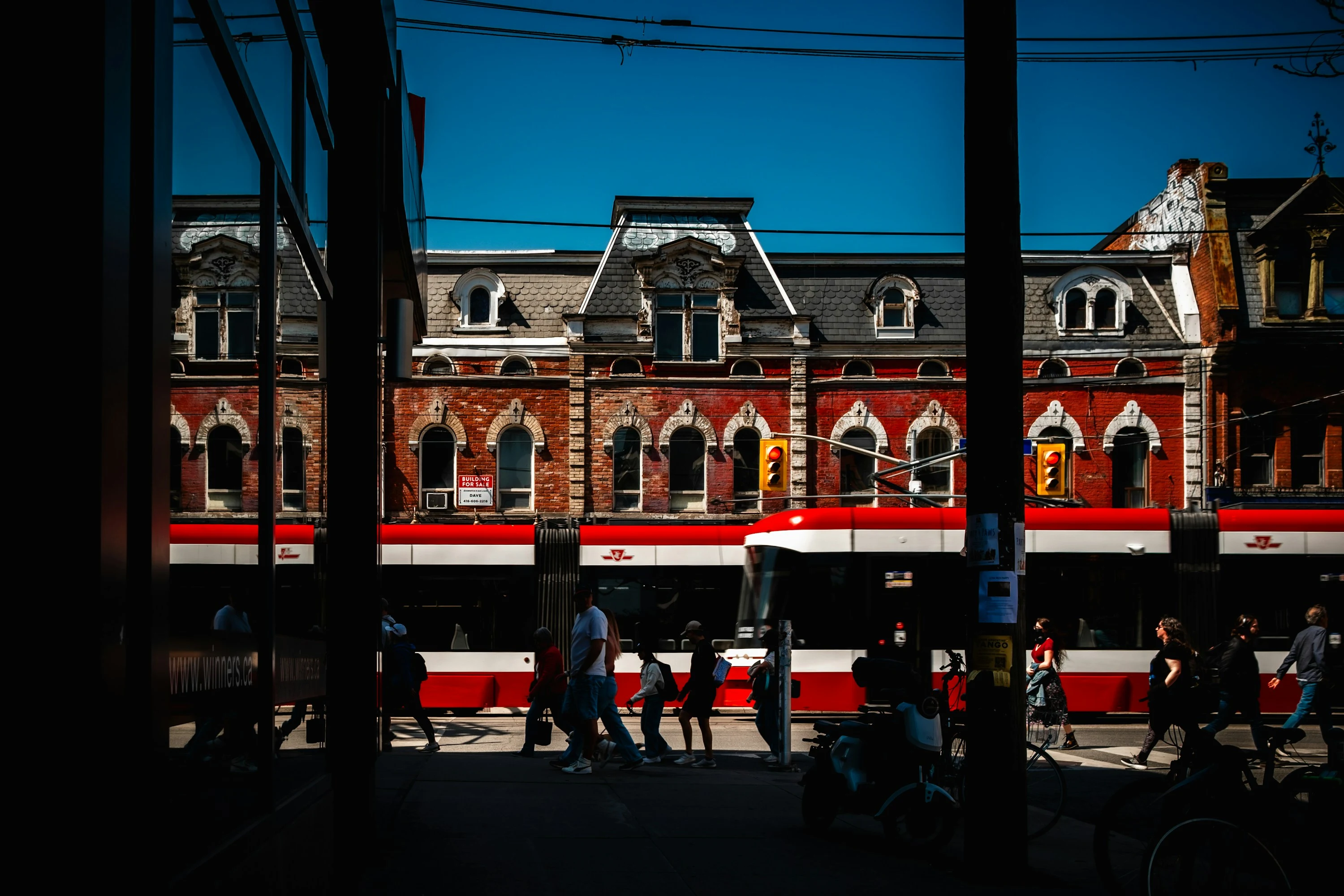 Bonde vermelho e pedestres passando diante de fachadas históricas de Toronto, entre luz e sombra.
