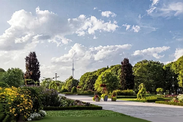 Jardim com canteiros floridos, árvores e a CN Tower ao fundo sob um céu com nuvens.